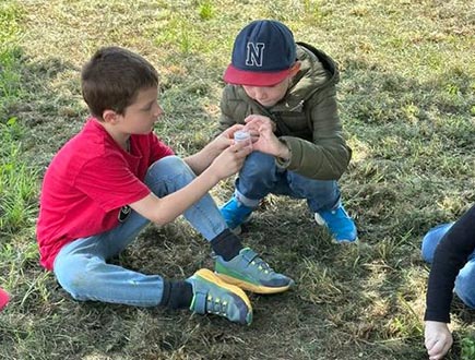 Kinder betrachten auf einer Wiese unter der Lupe gemeinsam ein kleines Tier mit großer Aufmerksamkeit.